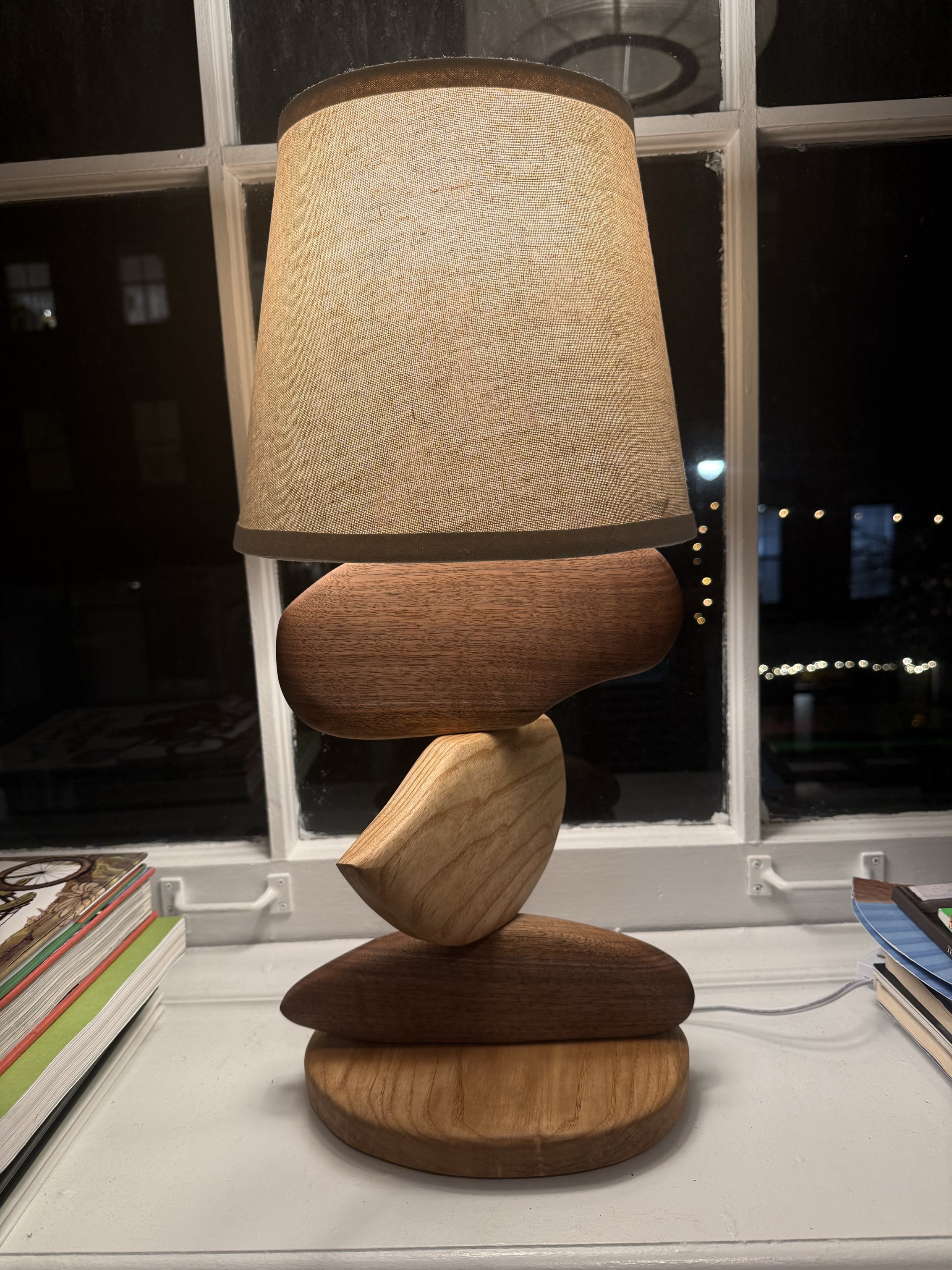 a table lamp made of stacked ash and walnut wood discs with a linen shade